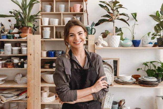Image of cute happy smiling young female ceramist standing in pottery studio.